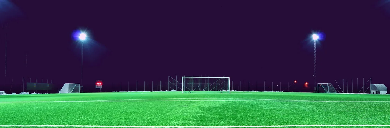Cancha de fútbol vacía iluminada por focos bajo un cielo nocturno violeta