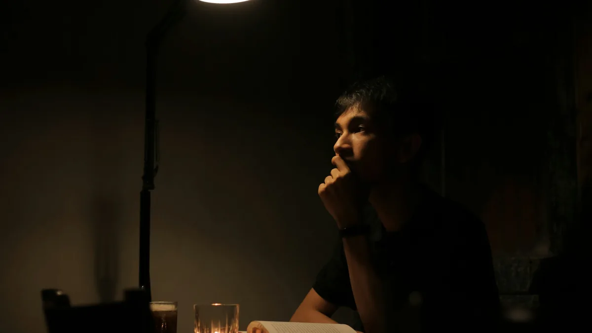 Una persona sentada sola a una mesa en una habitación en penumbra, pensando